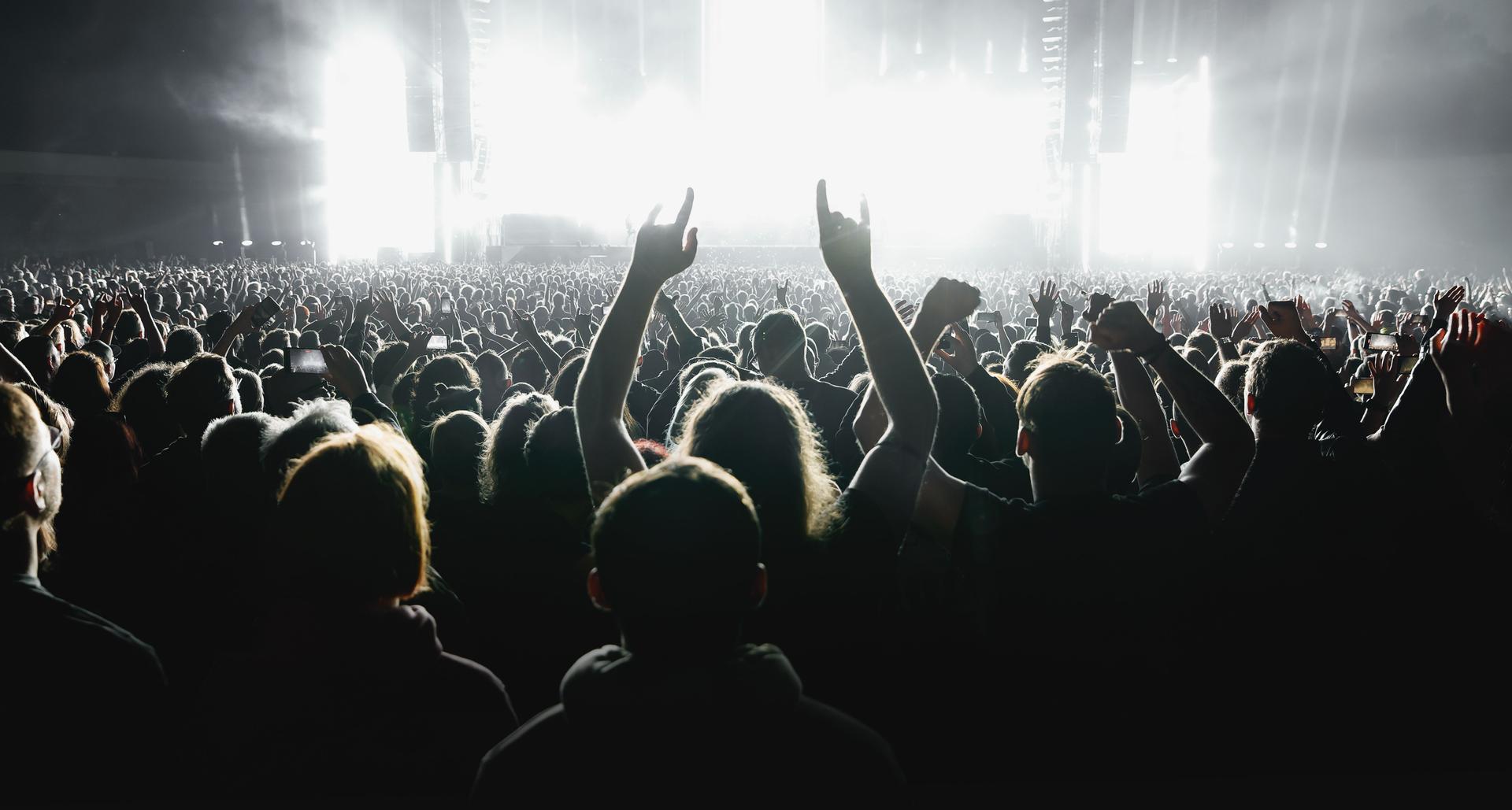 A lot of people raised up hands at the concert event. Fans arms against the stage light.